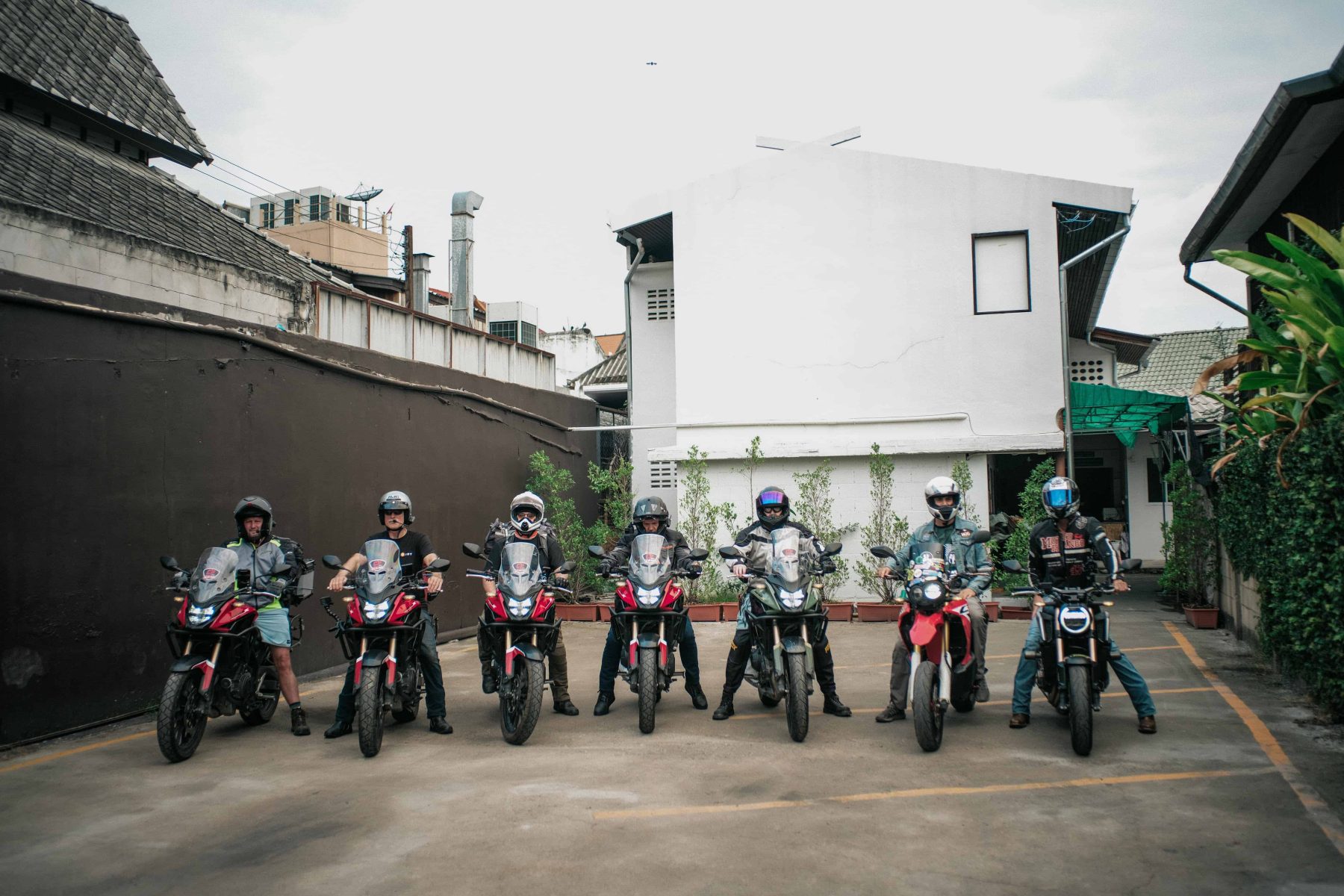 Group of motorcyclists lined up on different bikes, showcasing a variety of riding styles and motorcycle types