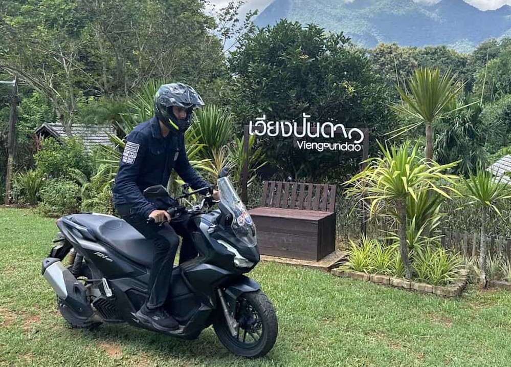Rider on scooter wearing Nexx X.WED3 adventure helmet, with mountains and greenery in the background