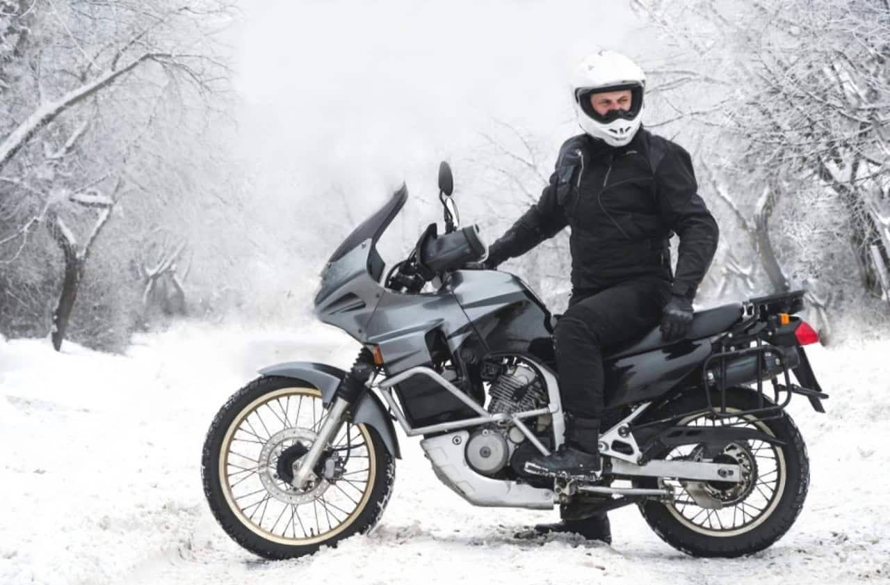 Motorcyclist in winter gear sitting on an adventure bike in snowy conditions, showing proper layering for cold-weather riding