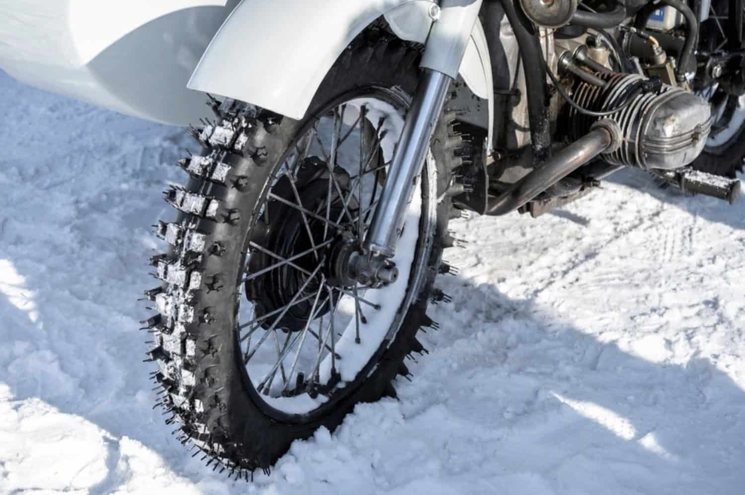 Close-up of a motorcycle tire with studs in snowy conditions, showing winter riding maintenance and preparation needs