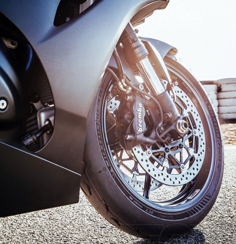 Close-up of a motorcycle front wheel with Michelin Power Cup 2 tire, showing tread and Brembo brakes on track