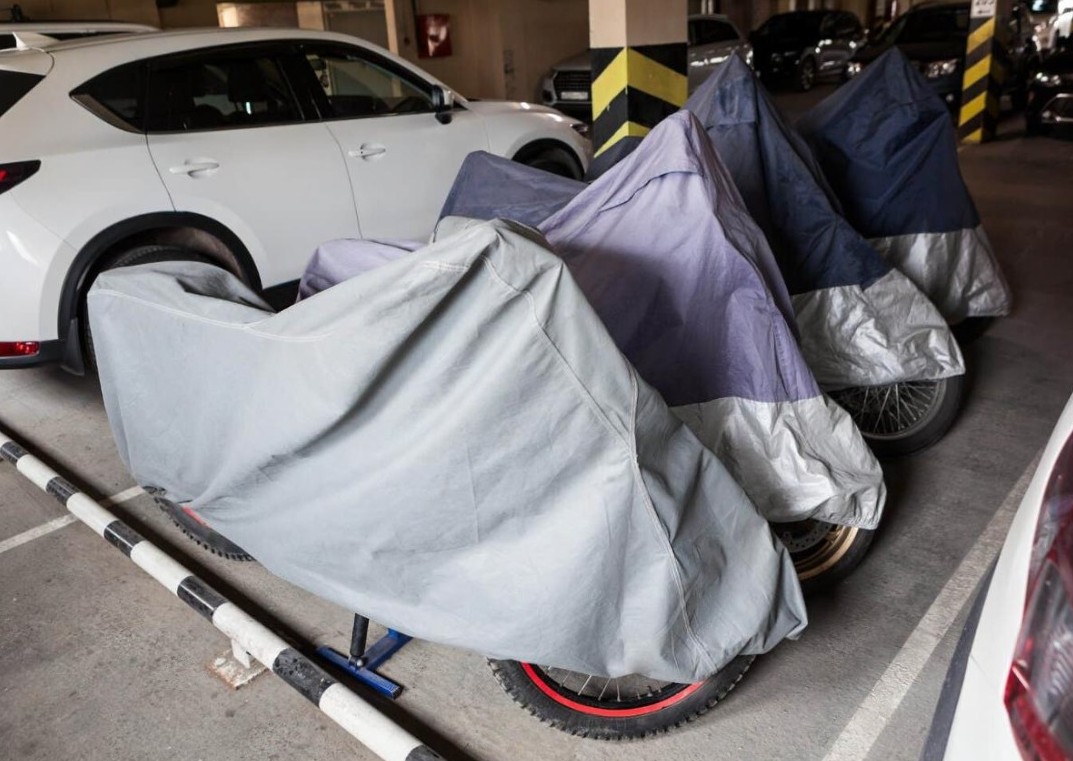 Motorcycles stored in a parking garage with breathable covers to prevent dust and moisture buildup.