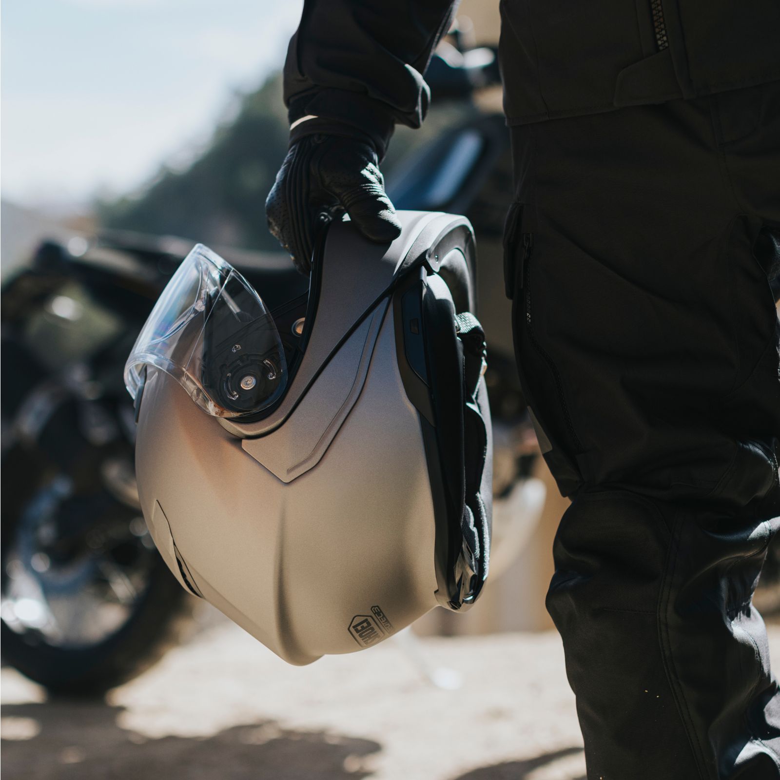 Shoei Neotec 3 modular helmet held by a rider in black gear outdoors