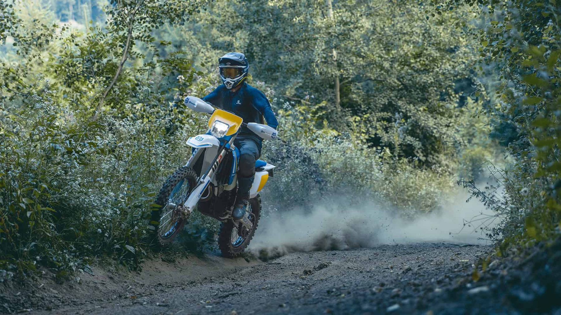 Rider on Husqvarna dual-sport motorcycle kicking up dust on forest trail