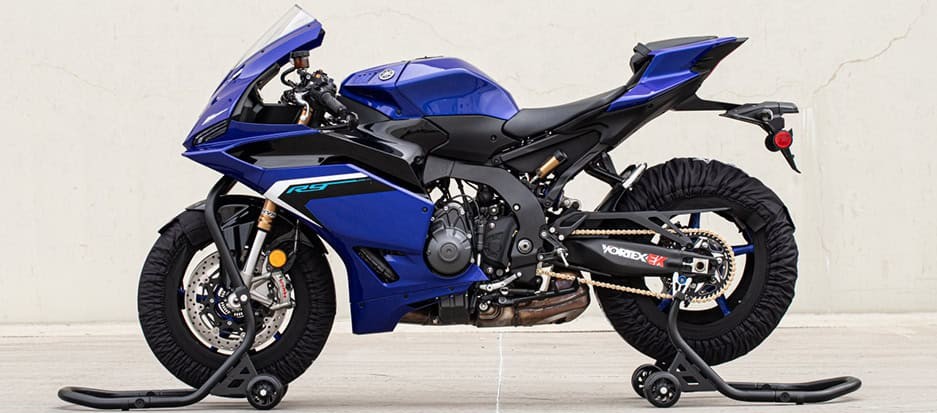 Blue Yamaha sportbike on Vortex front and rear stands with tire warmers, set up for storage or track prep.