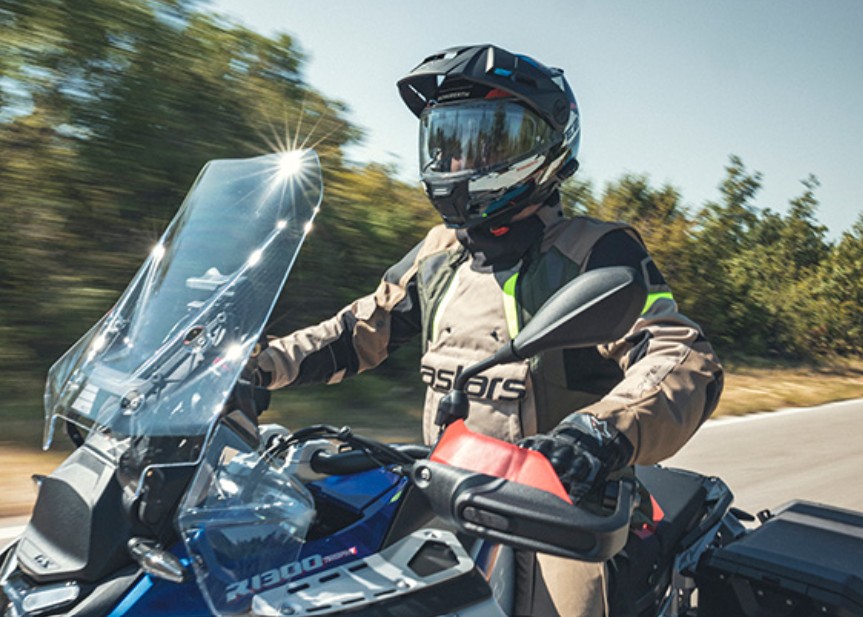 Rider wearing Schuberth E2 adventure helmet on a touring bike, showing its wide top scoop and chin vent design for airflow.