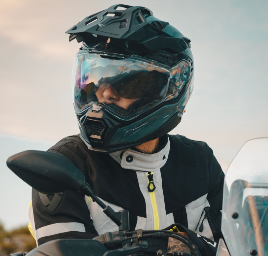 Rider wearing Nexx X.WED3 helmet with tinted visor and peak, on motorcycle at sunset