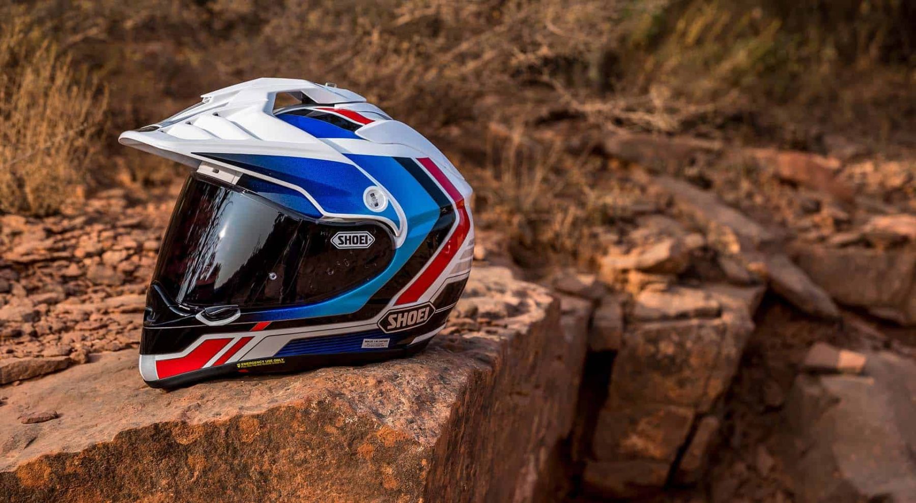 Shoei Hornet X2 adventure helmet with red, blue, and white graphics resting on desert rocks