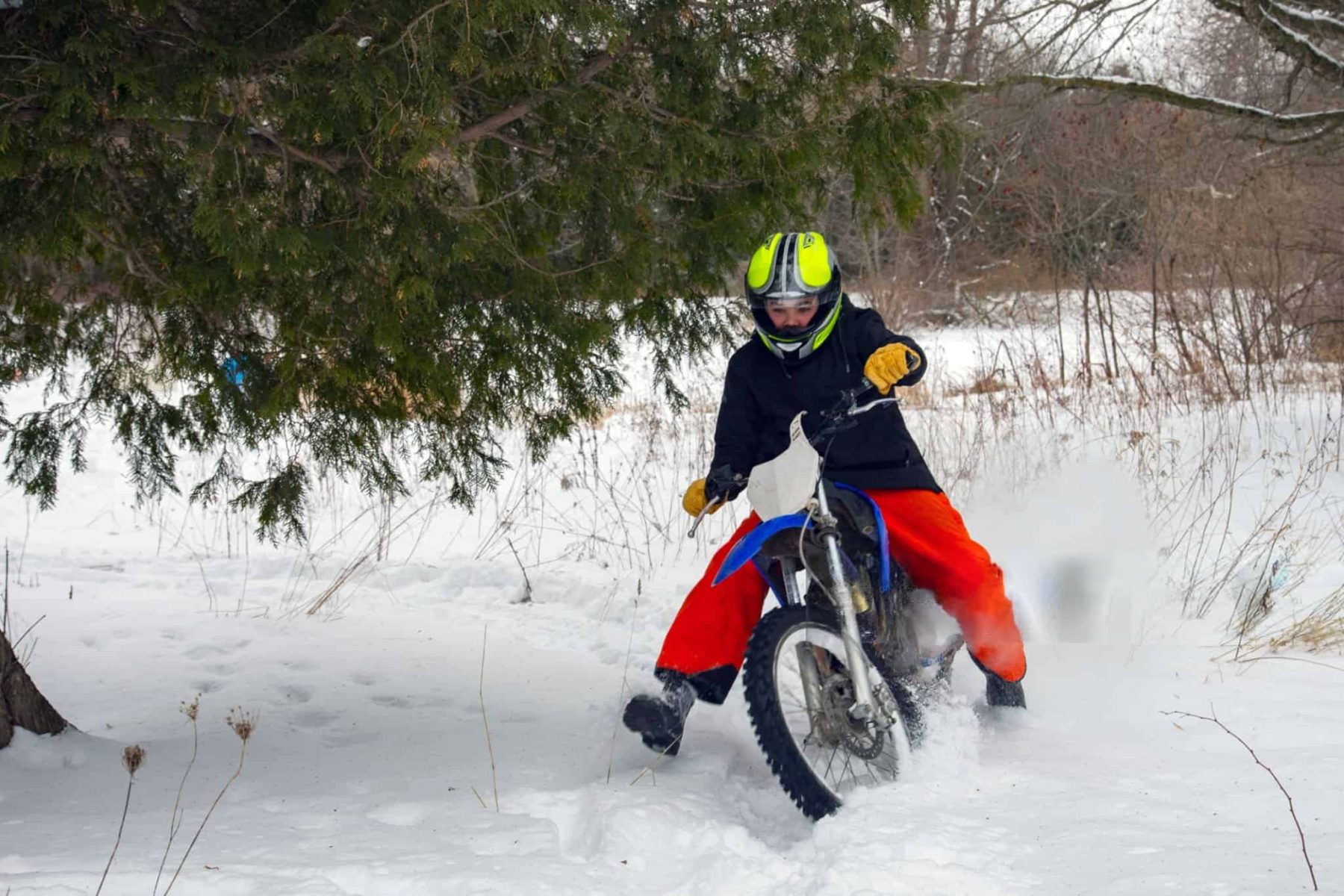Rider in bright gear on a dirt bike riding through snow, testing abrasion-resistant pants