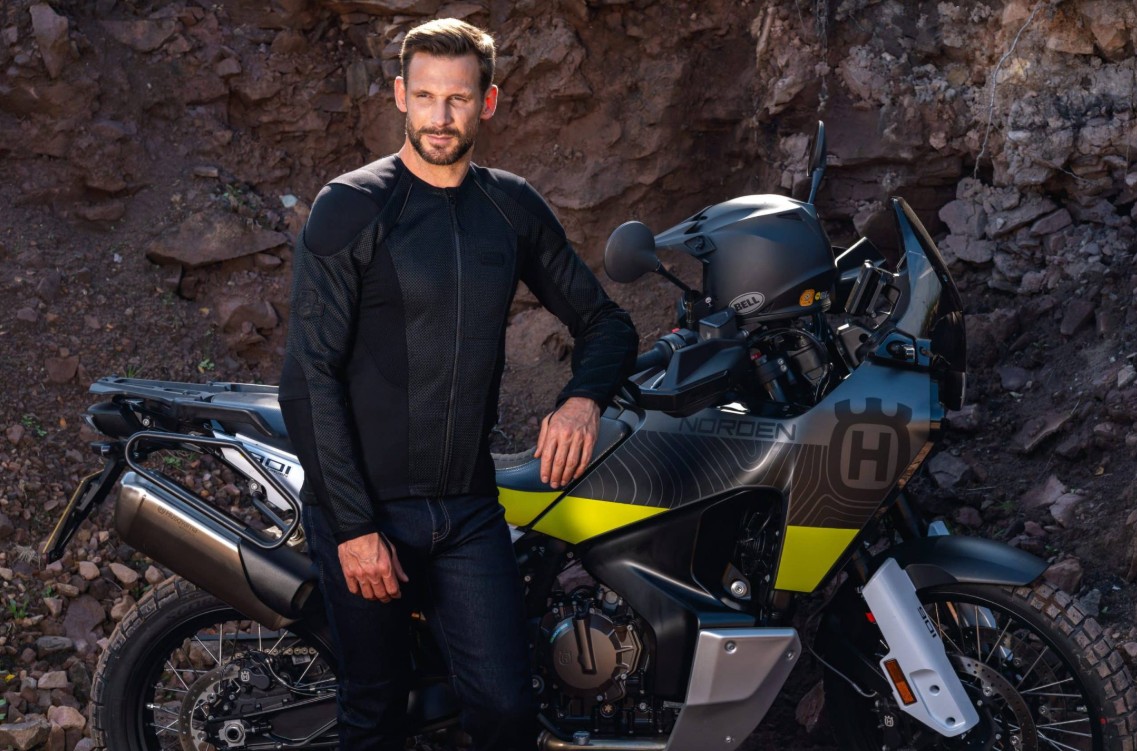 Rider wearing Knox armored shirt with fitted, jacket-like feel, paired with jeans beside an adventure motorcycle