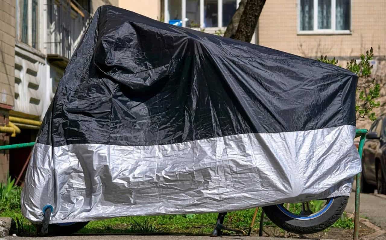 Motorcycle stored outdoors under a two-tone cover protecting it from weather.
