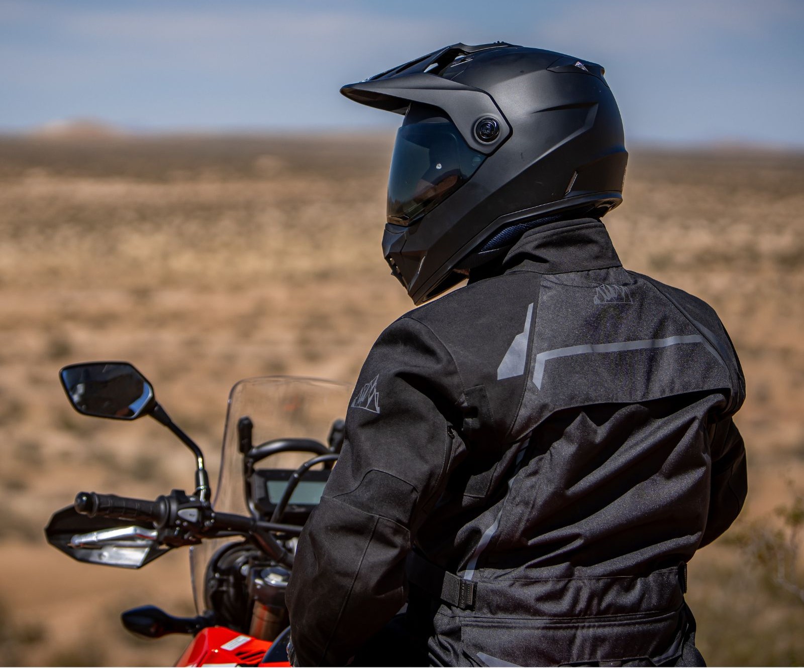 Rider in black Tourmaster Highlander jacket and helmet on an ADV bike in the desert.