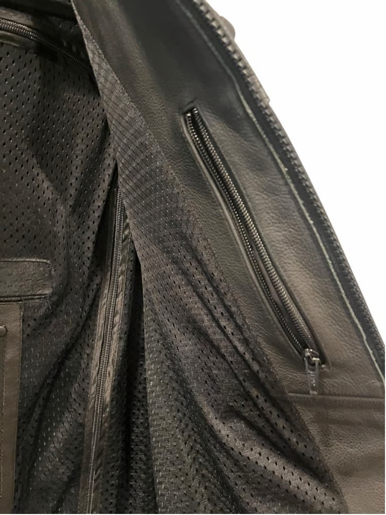 Close-up view of a leather motorcycle vest interior showing zippered pockets and mesh lining for concealed storage.
