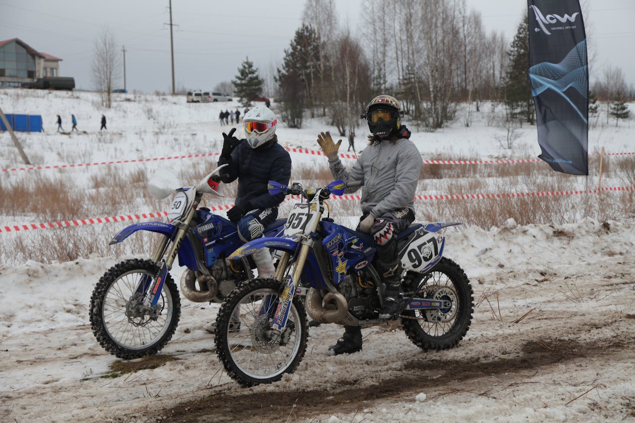 Two riders on dirt bikes in snowy terrain, showing winter motorcycle riding with proper gear and preparation