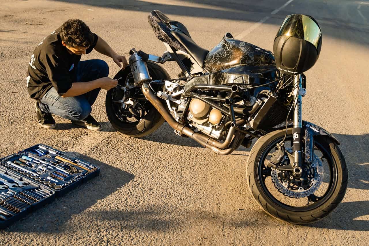 Rider working on motorcycle rear wheel with a full tool kit laid out on the ground