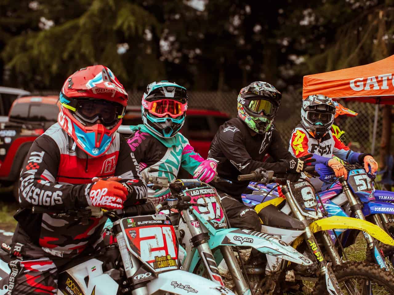 Group of motocross riders in colorful helmets and goggles lined up on dirt bikes before a race