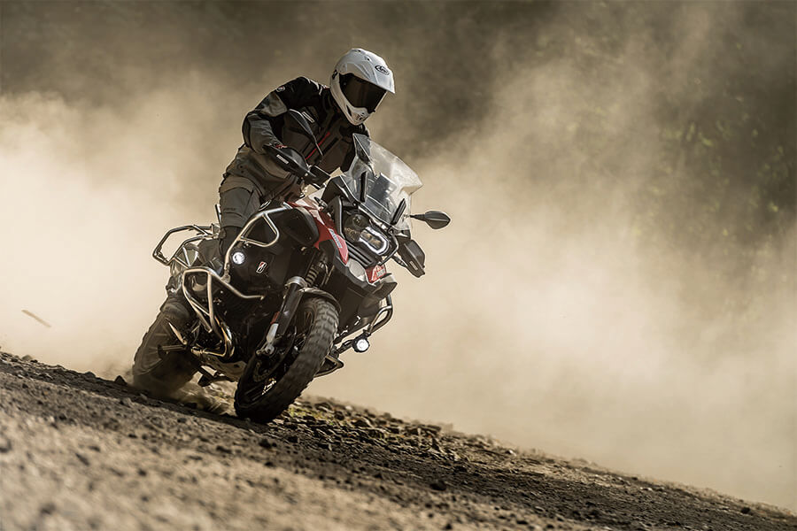 Rider leaning BMW adventure bike shod with Bridgestone AX41 tires on dusty trail