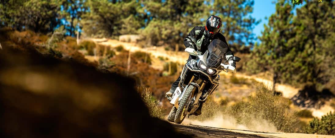 Adventure rider on a dual-sport bike with Dunlop Trailmax Mission tires kicking up dust on a dirt road