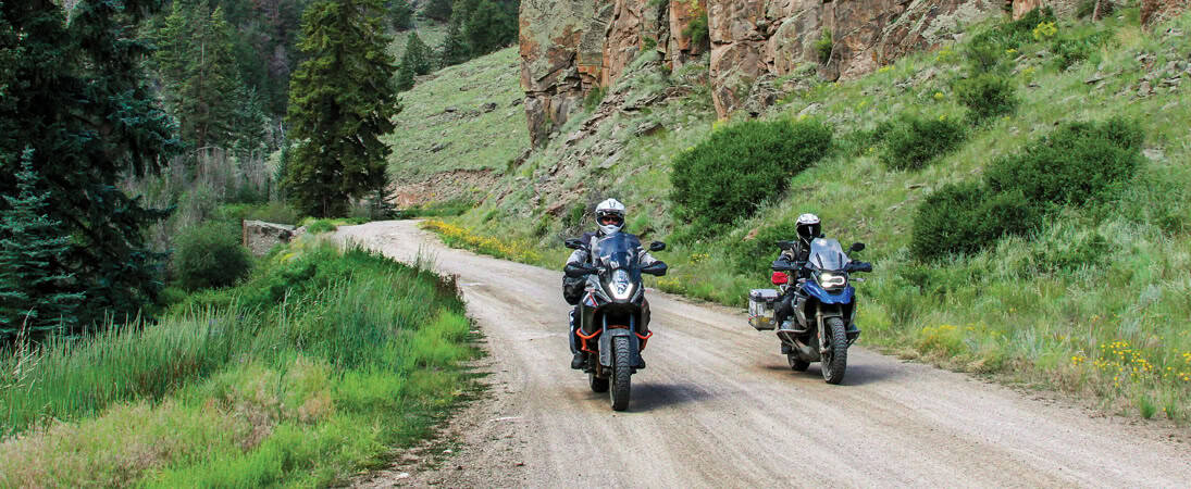 Two adventure motorcycles riding on a gravel mountain road with dual-sport tires
