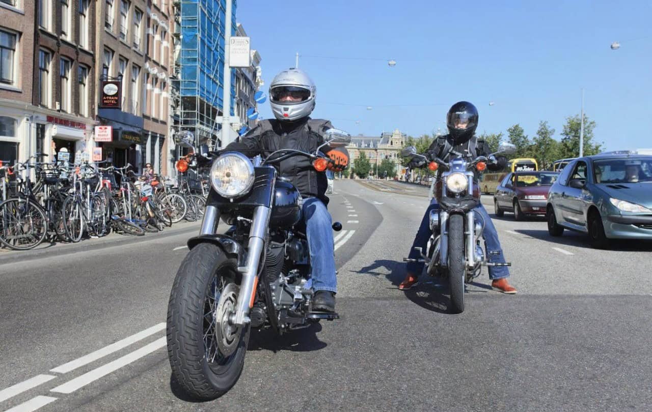 Two riders cruising city streets on V-twin motorcycles, representing power and durability supported by Amsoil 20W-50 Synthetic Oil