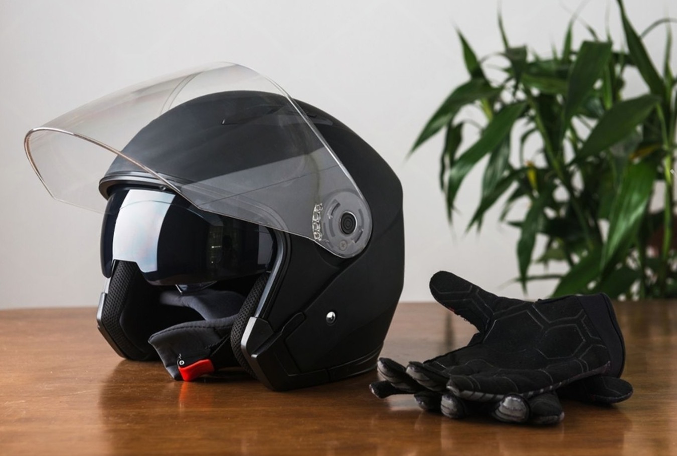 Open-face smart helmet on a table beside gloves, showing built-in visor and comms-ready design.