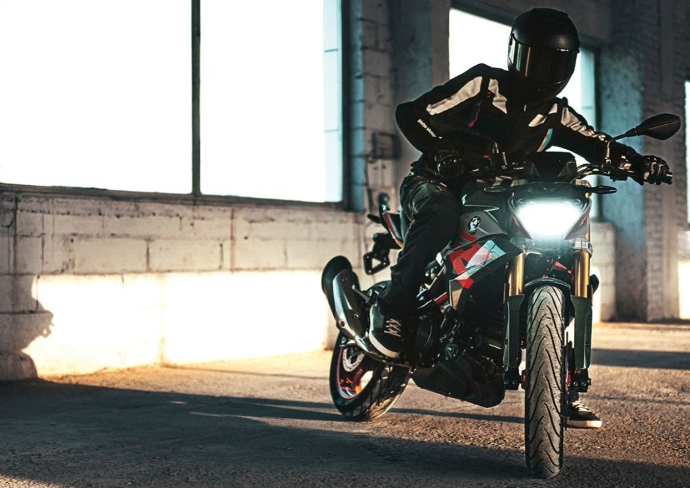 Motorcyclist on a BMW G 310 R balancing in a sunlit industrial space, showcasing light weight and agility