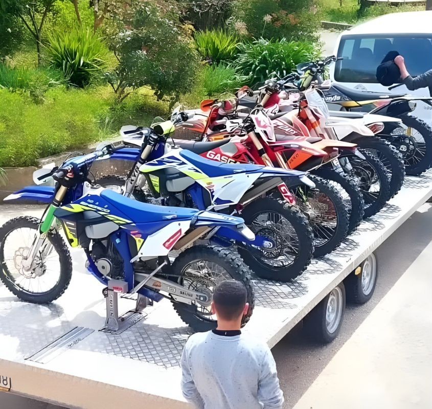 Several dirt bikes secured on a flatbed trailer using wheel chocks, ready for transport to a riding destination.