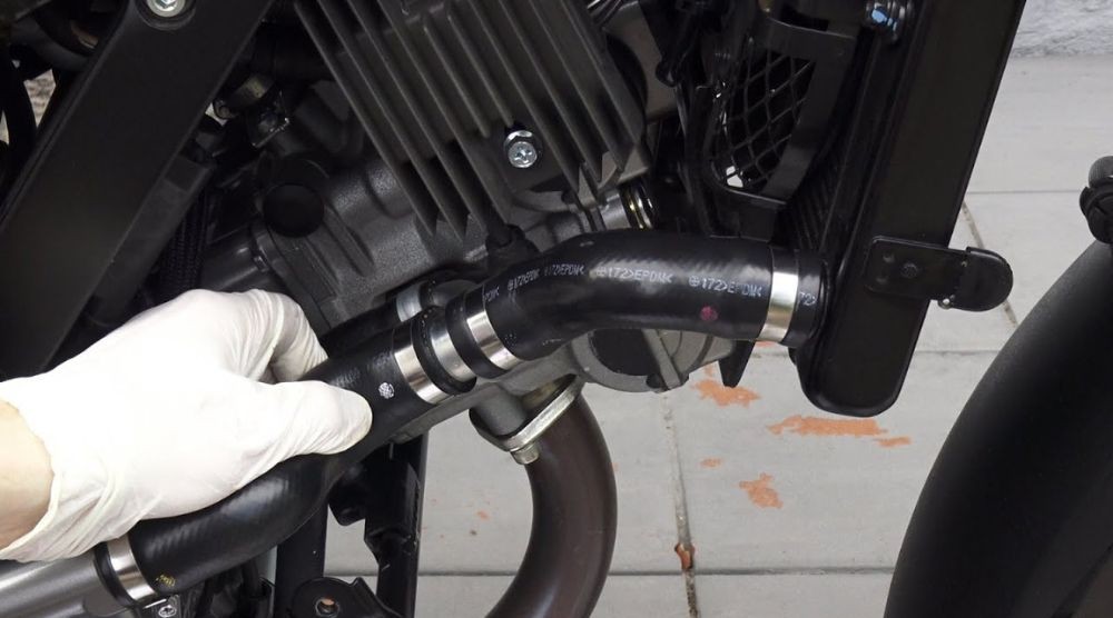 Mechanic wearing gloves inspecting motorcycle radiator hose for cracks and pressure seal