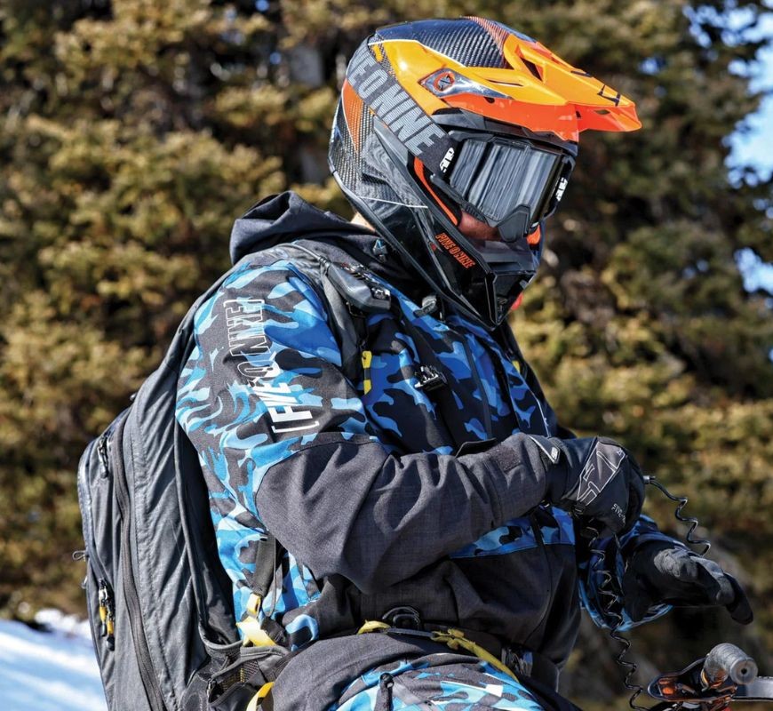 Rider wearing the 509 Forge Insulated Jacket in blue camo, geared up for cold off-road riding with helmet and gloves in snowy terrain