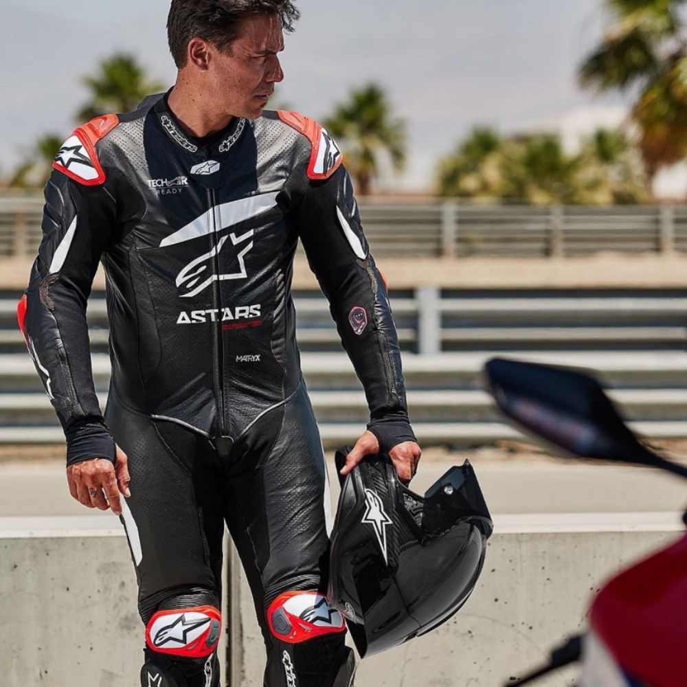 Rider wearing the Alpinestars GP Plus V4 race suit in black with red accents, showing its Flex Plus leather and ergonomic stretch panels.