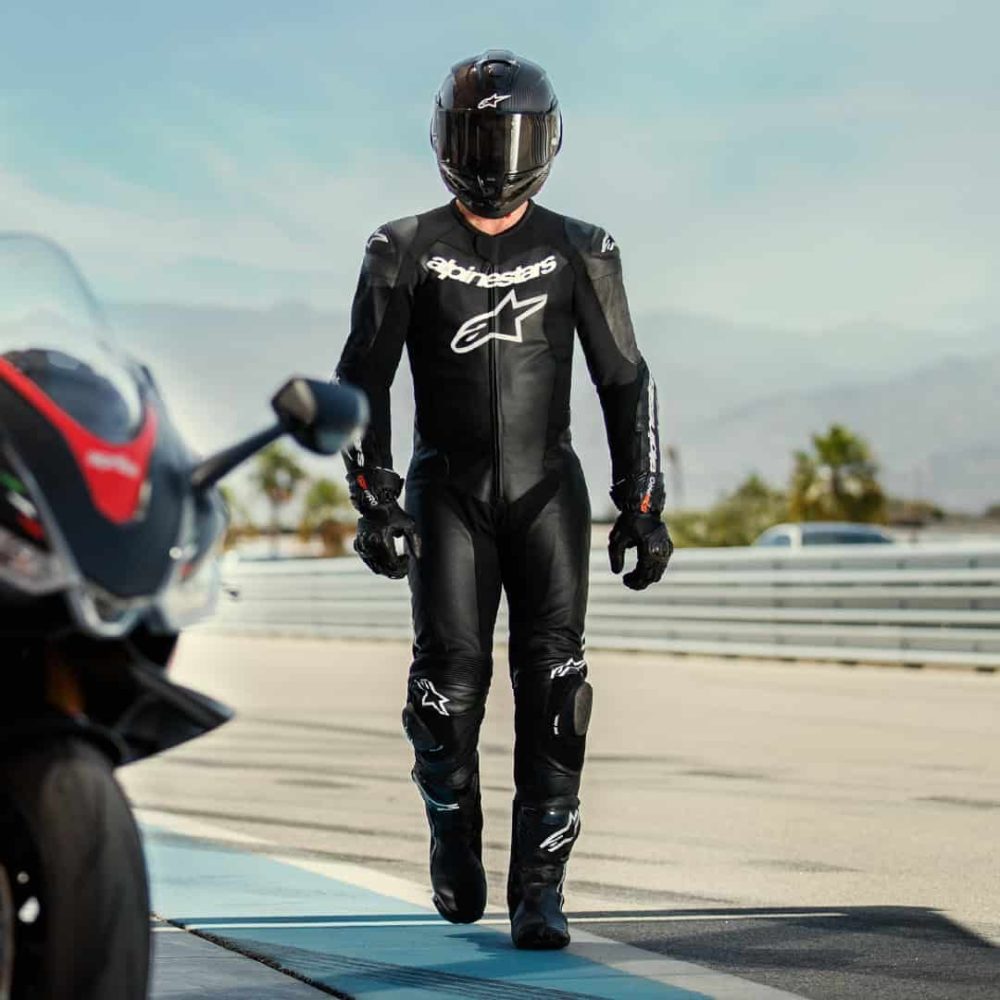 Rider in full black Alpinestars Missile V2 race suit walking along a racetrack, showing its streamlined fit and Tech-Air-ready design.