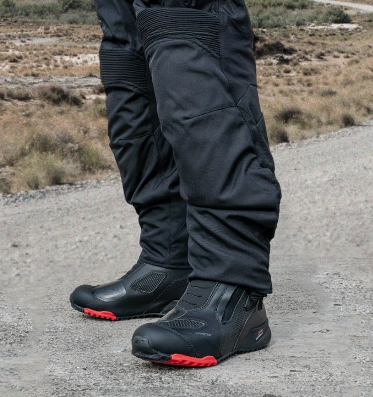 Rider wearing Alpinestars RT-7 Drystar boots standing on a dirt road, showcasing their mid-height touring design.