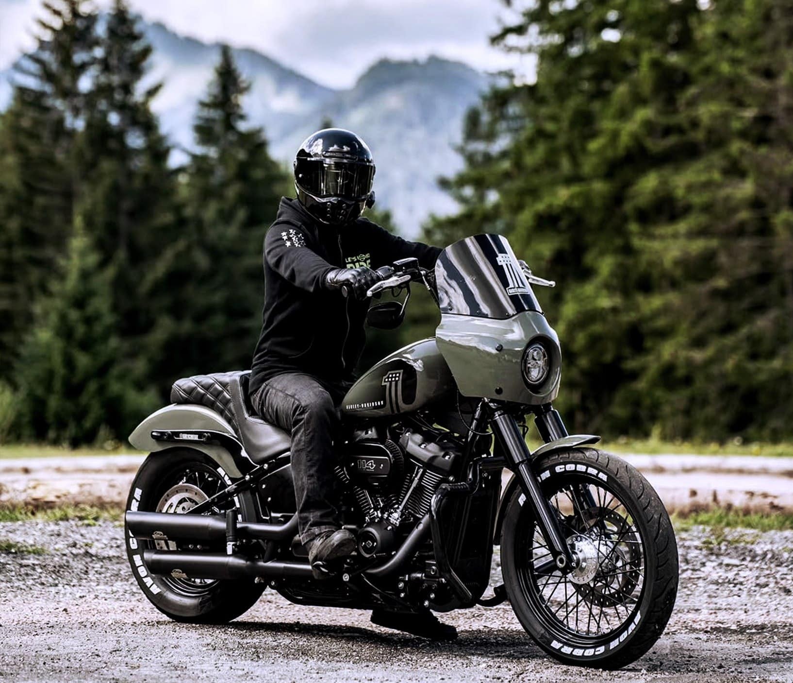 Motorcyclist on a custom cruiser equipped with Avon Cobra Chrome tires in a scenic mountain setting.