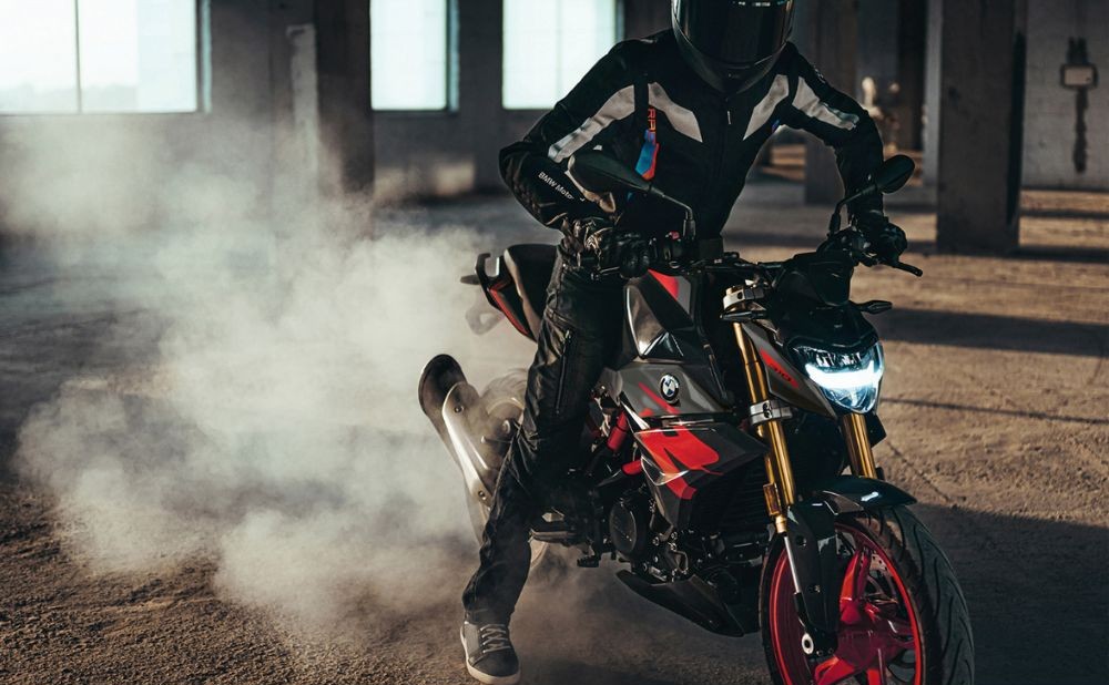 Rider performing a burnout on a BMW G 310 R motorcycle inside an industrial warehouse