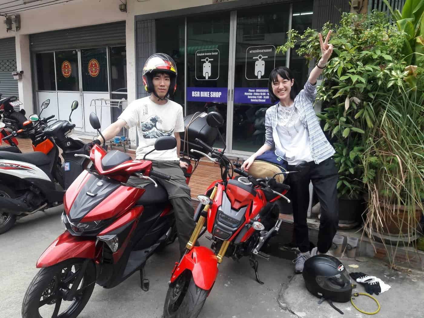 Two happy renters posing with scooters outside BSR Bike Shop in Bangkok’s Phra Khanong district, ready to explore Thailand on two wheels