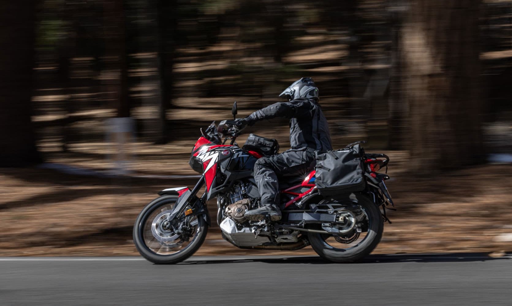 Adventure rider in full touring gear on a red motorcycle, cruising through forest roads at speed, showcasing comfort and protection
