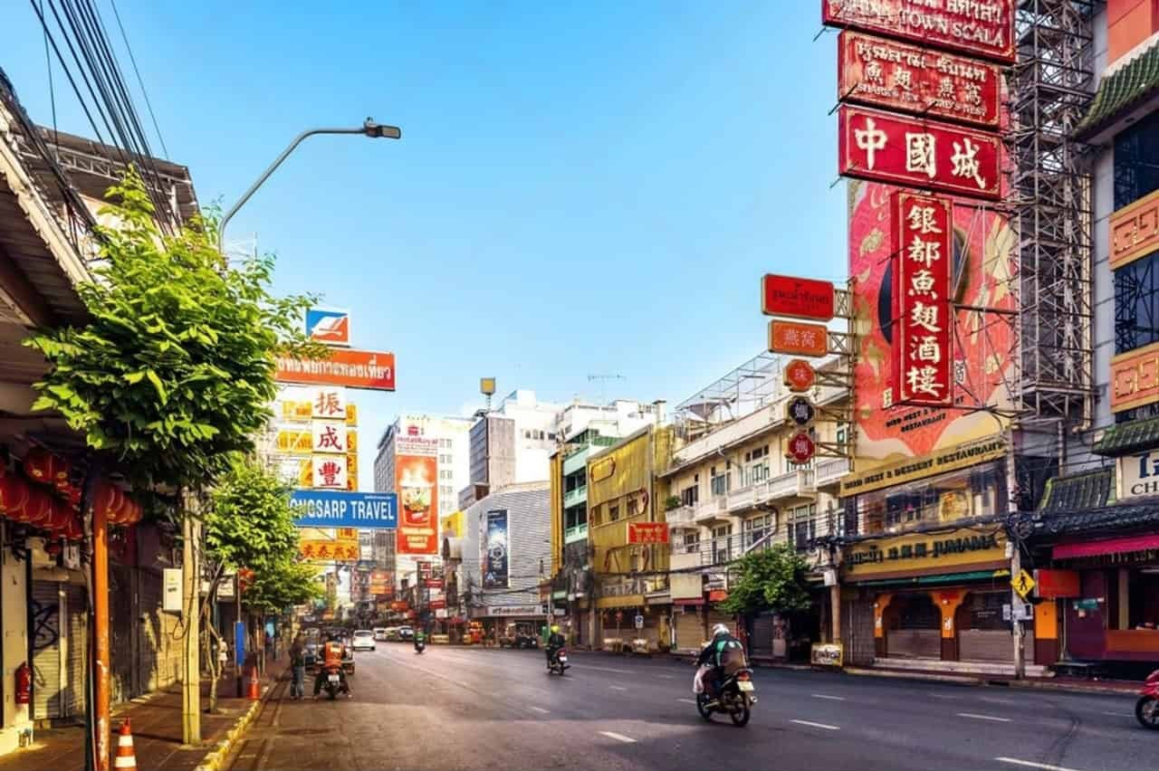 Motorcyclists riding through Bangkok’s Chinatown, surrounded by colorful shop signs and early morning city light