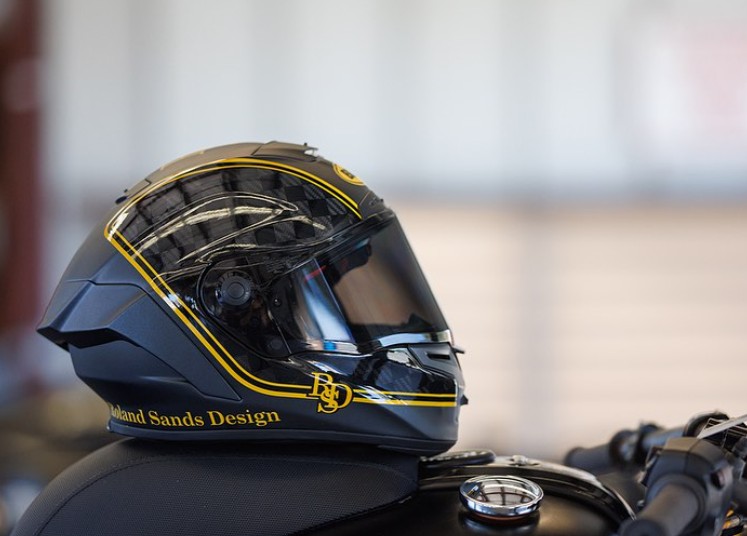 Close-up of a Roland Sands Design full-face motorcycle helmet with a tinted visor, resting on a black bike and reflecting ambient light.