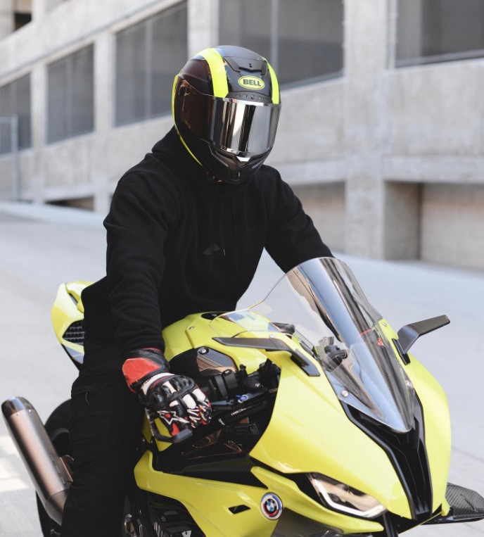 Rider wearing a Bell Race Star DLX Flex helmet on a yellow sportbike, showing its carbon-shell design and sleek street-race aesthetic.
