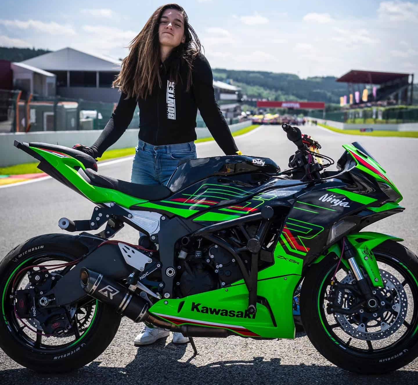 Woman wearing a Bowtex base layer top standing beside a green Kawasaki Ninja, showing how protective layers can pair with casual gear.