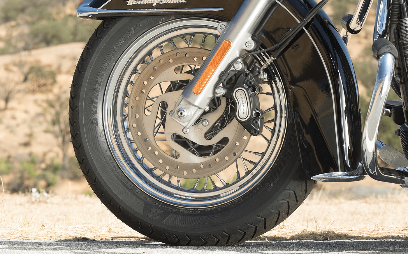 Close-up of a cruiser front wheel equipped with Bridgestone Battlecruise H50 tire showing tread and brake detail.