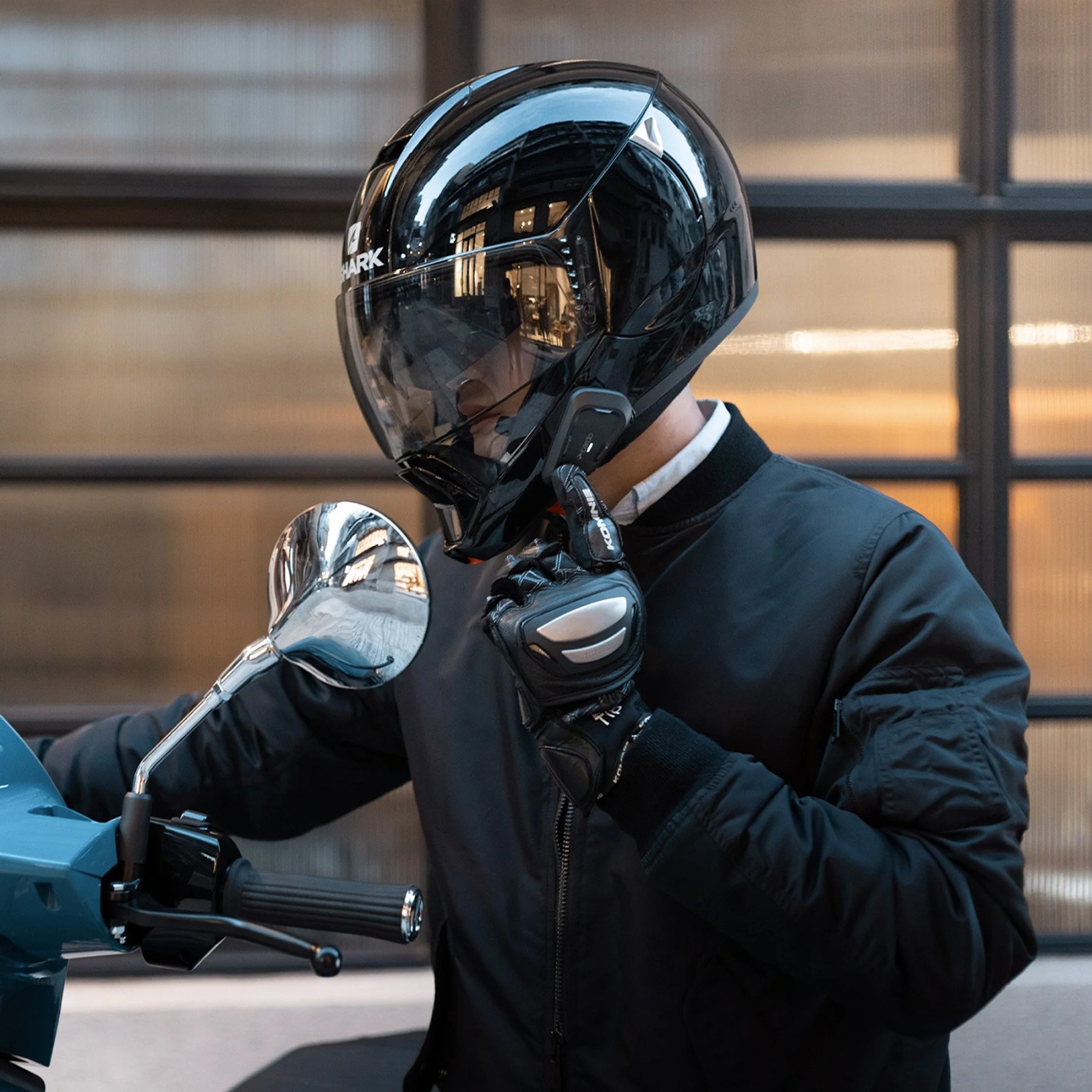 Rider wearing a glossy black full-face helmet with a Cardo Spirit HD communicator, preparing to ride a scooter in the city.