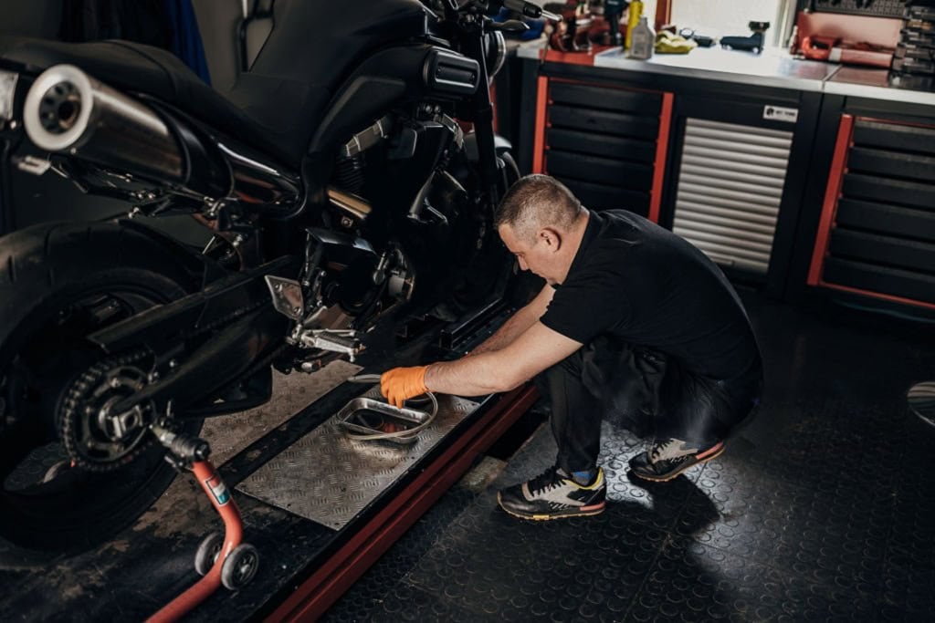 Mechanic performing motorcycle maintenance using a rear paddock stand in a garage