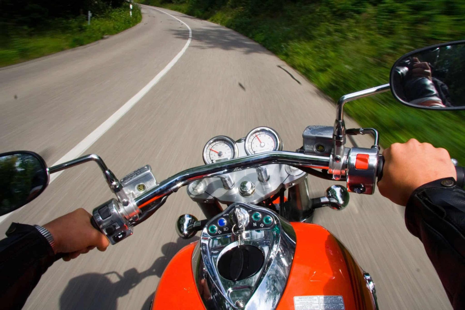 First-person view of a rider’s hands on motorcycle handlebars while cruising a curved road, showing grip reach and hand position.