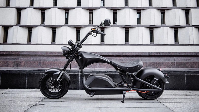 Eahora M1PS electric chopper motorcycle parked in front of a modern concrete building