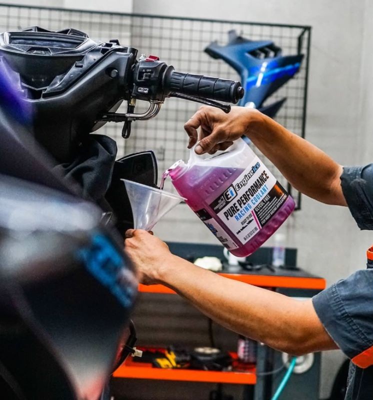 Mechanic pouring Engine Ice Pure Performance Racing Coolant into motorcycle radiator using a funnel