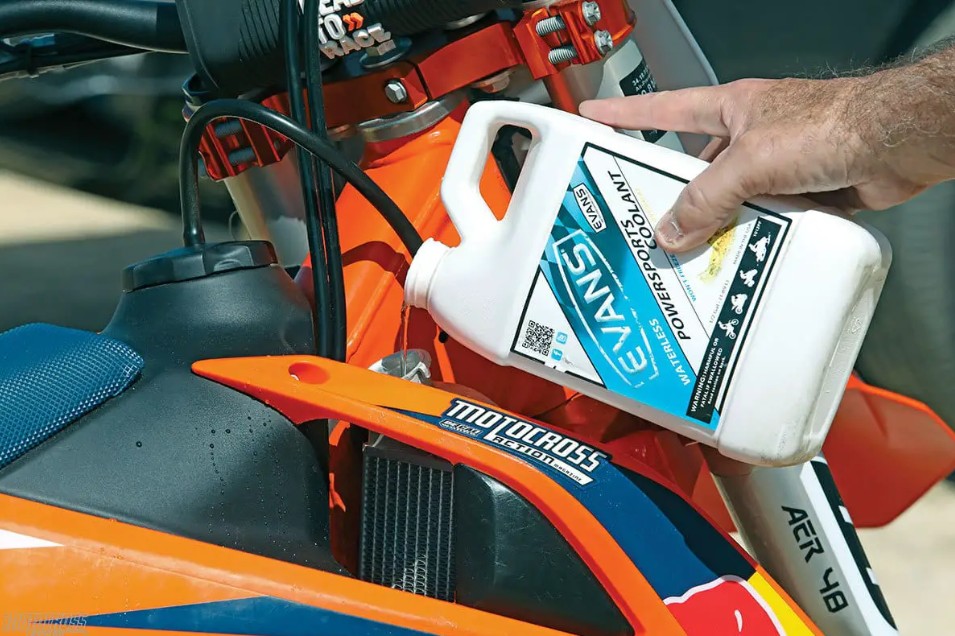 Mechanic pouring Evans Powersports Waterless Coolant into an orange motocross bike radiator outdoors