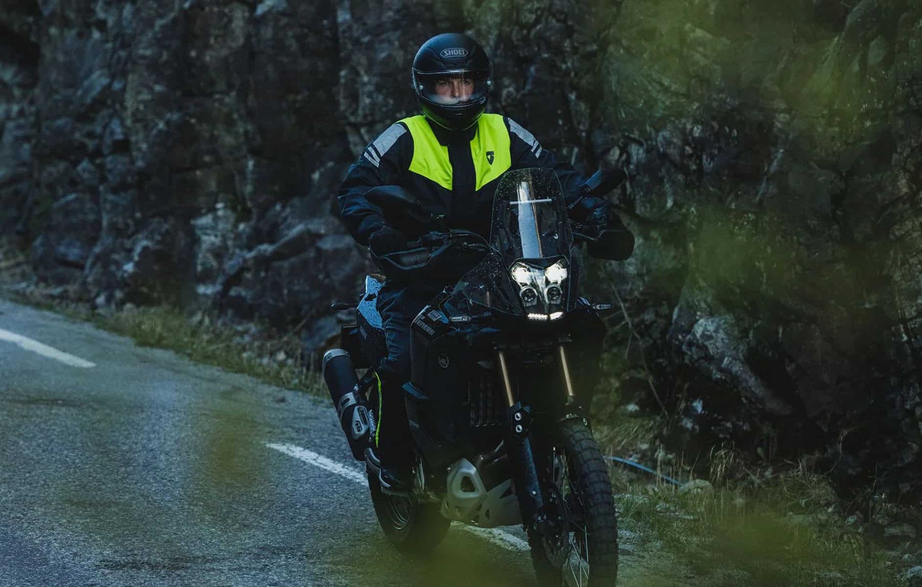 Motorcyclist wearing REV’IT! Pacific 4 H2O one-piece rain suit riding through wet mountain roads