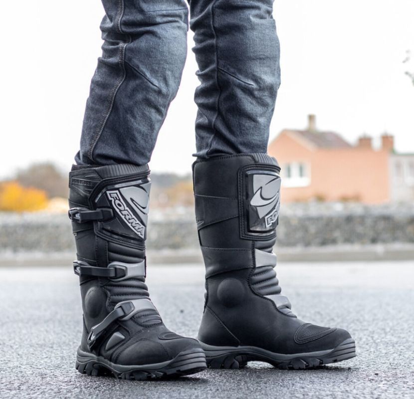 Close-up of a rider wearing Forma Adventure Boots, standing on wet pavement, showing rugged design and dual-buckle closure.