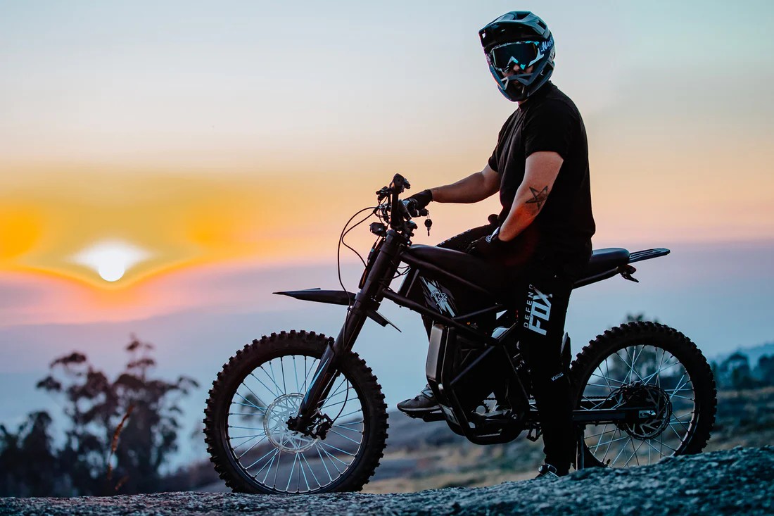 Rider sitting on an electric dirt bike at sunset, highlighting seating comfort and fit